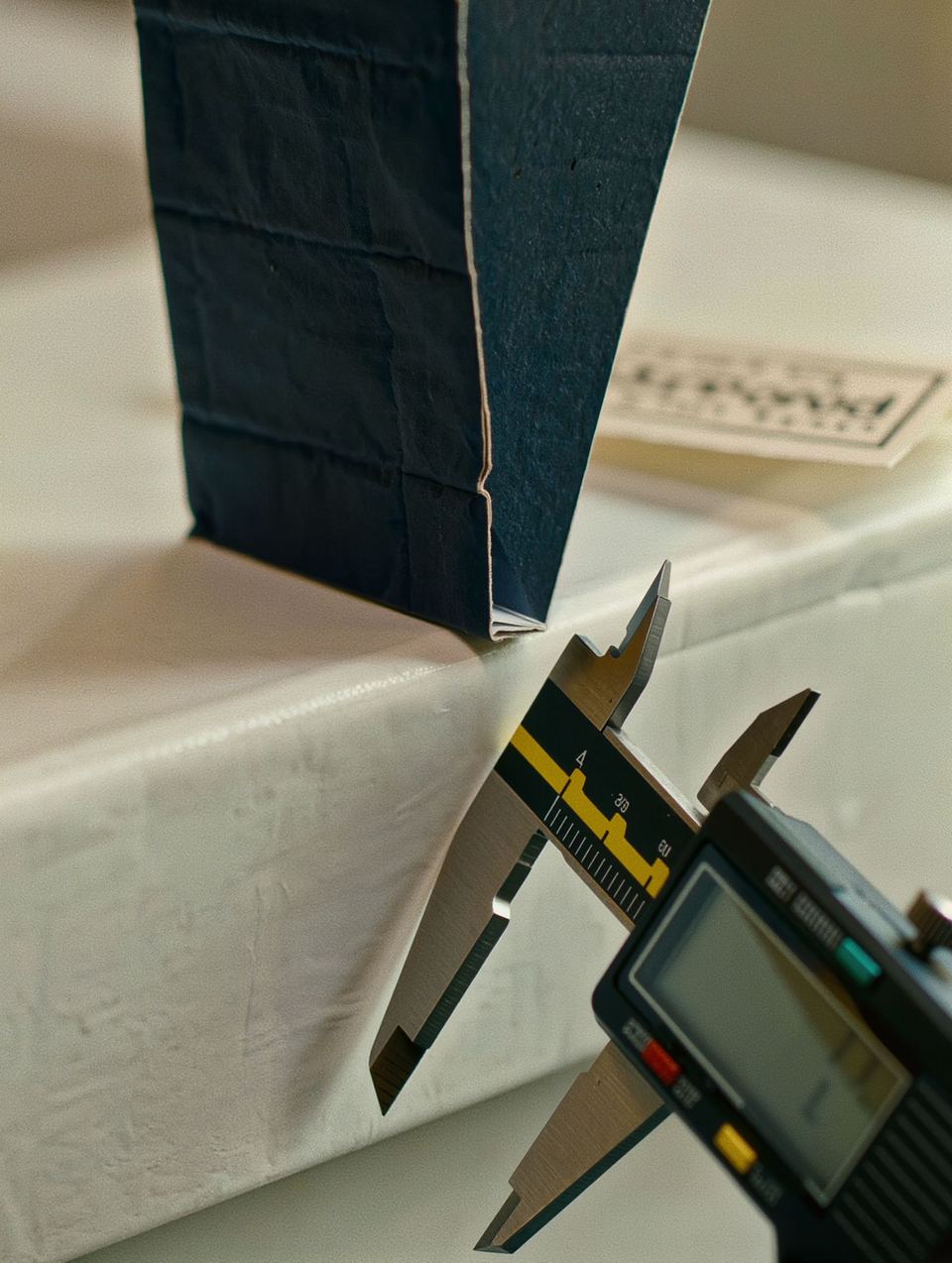 A digital caliper measuring the wall of a navy rigid box lid